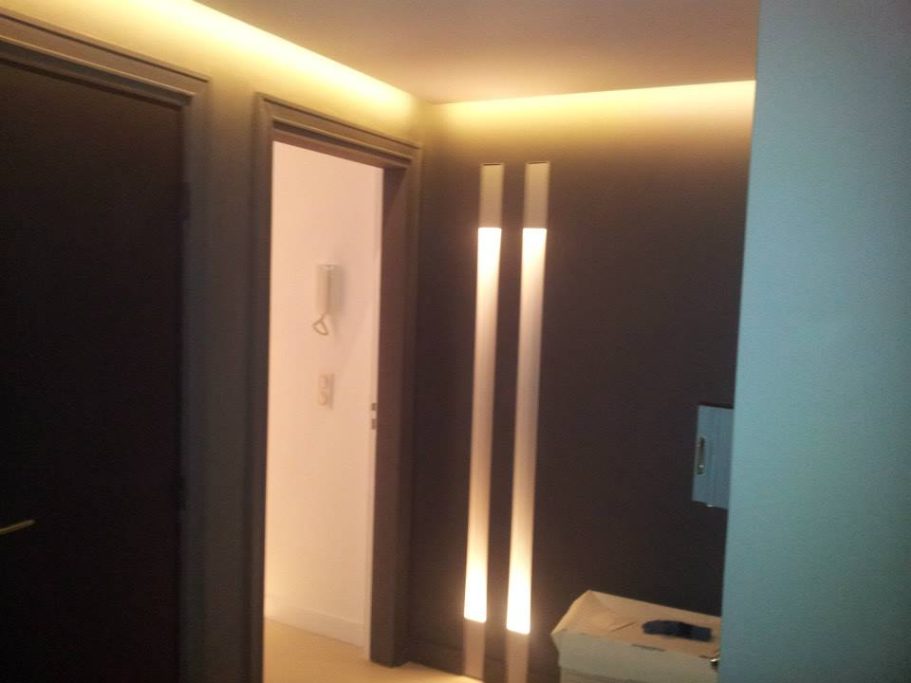 Hallway avec éclairage discret et portes sombres, meuble blanc à droite.