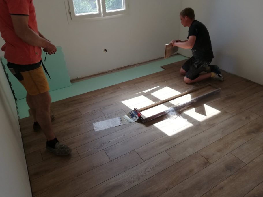 Deux personnes posent un revêtement de sol en bois dans une pièce lumineuse.