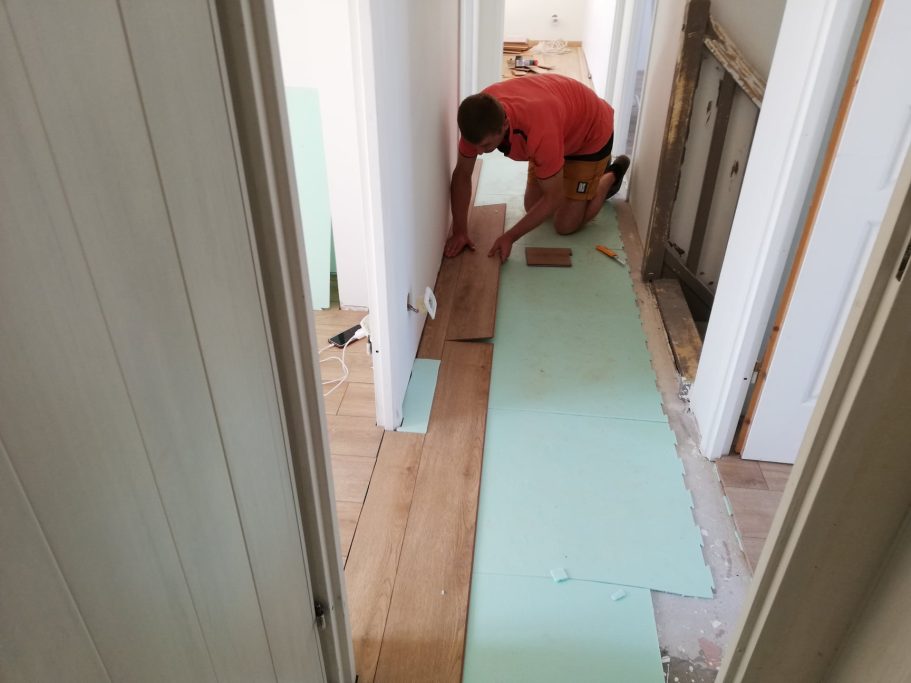 Un homme pose des bandes de revêtement de sol dans un couloir en cours de rénovation.