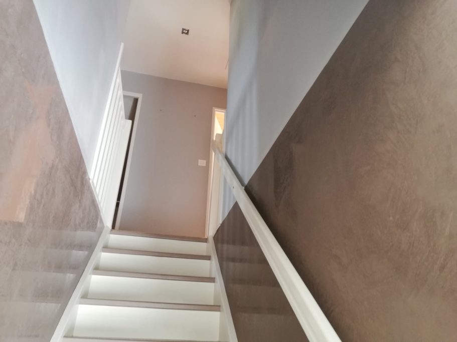 Escalier menant à une porte au bout d'un couloir éclairé. Walls gris clair.