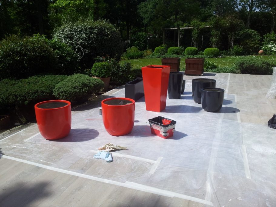 Des pots de fleurs rouges et noirs disposés sur un sol en pierre dans un jardin.