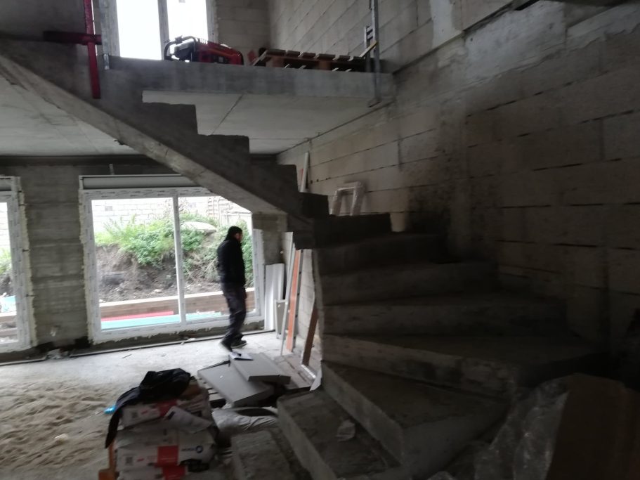 Escaliers inachevés dans un chantier, avec une personne debout près de la fenêtre.